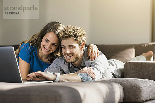 Lächelndes Paar mit Laptop auf dem Sofa zu Hause liegend