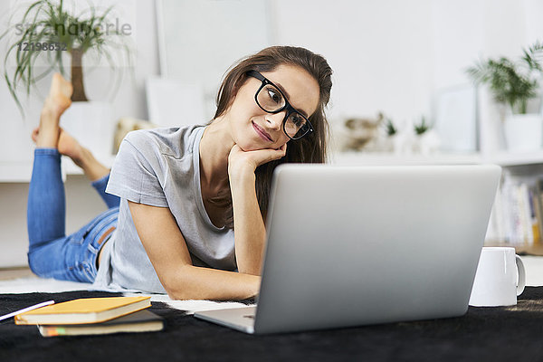 Junge Frau zu Hause auf dem Boden liegend mit Laptop
