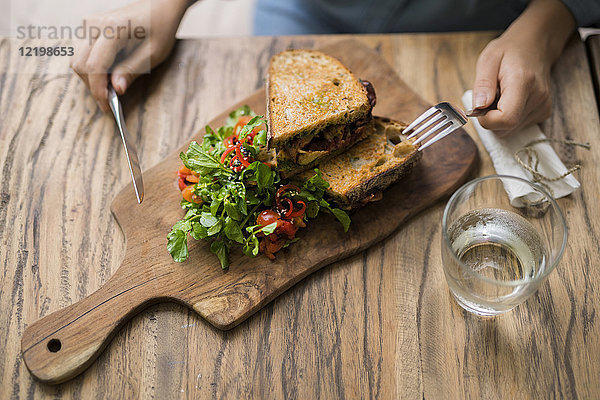 Hände halten Messer und Gabel am Holztisch mit verziertem Salat und knusprigem Brot