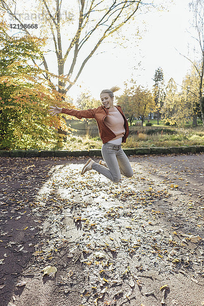 Fröhliche junge Frau beim Springen in der Luft im herbstlichen Park