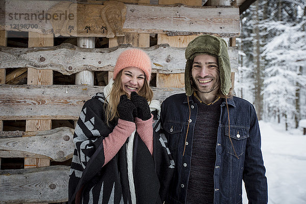 Porträt eines glücklichen Paares vor einem Holzhaufen im Freien im Winter