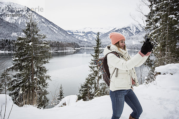 Junge Frau bei einem Selfie in alpiner Winterlandschaft mit See