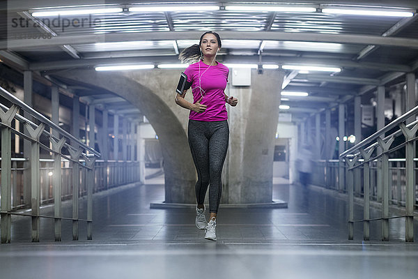 Junge Frau im rosa Sportshirt läuft nachts in moderner U-Bahn-Station