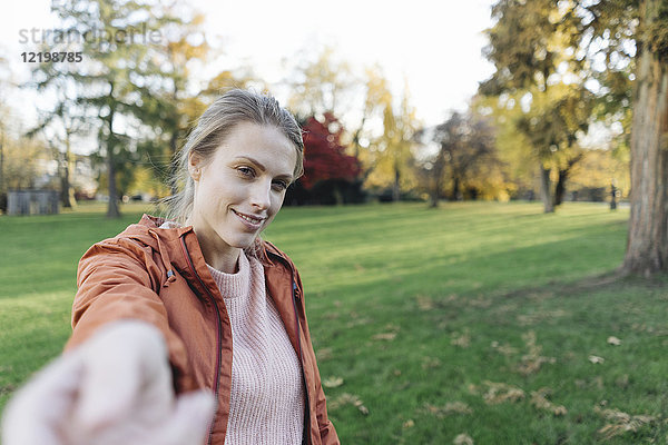 Porträt einer jungen Frau  die im herbstlichen Park die Hand ausstreckt.
