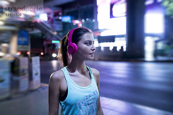 Junge Frau in rosa Sportshirt in moderner urbaner Umgebung bei Nacht