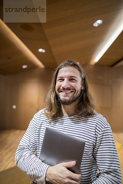 Porträt des lachenden Mannes mit Laptop in der Universität