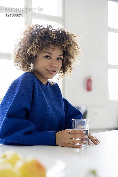 Porträt einer lächelnden jungen Frau mit einem Glas Wasser am Tisch