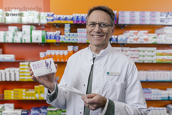 Porträt eines lächelnden Apothekers mit Tablettenpackung und Rezept in der Apotheke