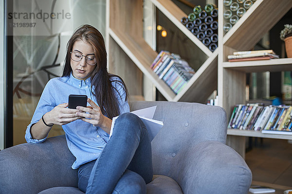 Junge Frau sitzt im Cafe mit Smartphone