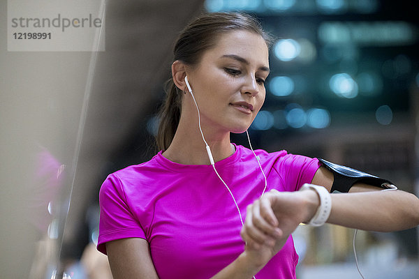 Junge Frau in rosa Sportshirt hört Musik und überprüft ihre smartwatch