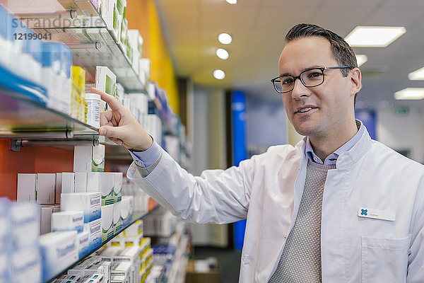 Porträt eines lächelnden Apothekers mit Medikamenten im Regal in der Apotheke