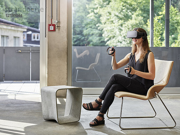 Lächelnde Frau mit VR-Brille auf dem Stuhl sitzend