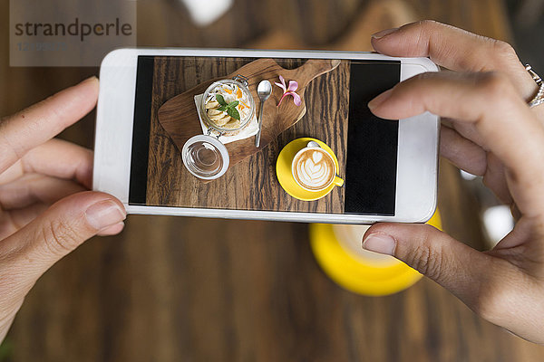 Frauenhände beim Fotografieren von Müsli und Kaffee mit dem Smartphone
