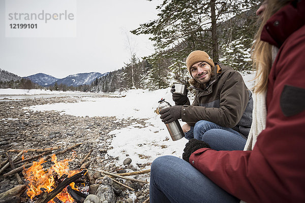 Paar auf einer Reise im Winter bei einem heißen Getränk am Lagerfeuer
