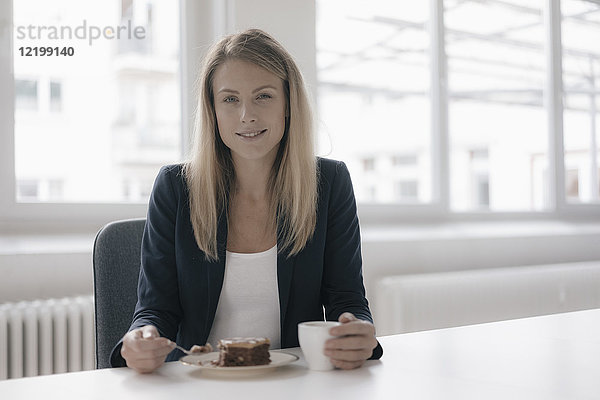 Porträt einer lächelnden Geschäftsfrau bei Kaffee und Kuchen am Schreibtisch im Büro