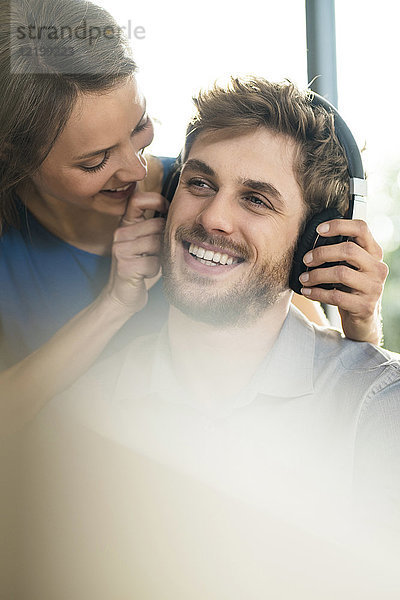 Lächelnde Frau setzt Kopfhörer auf Freund auf