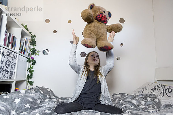Lächelndes Mädchen auf dem Bett  das mit Teddybär spielt.