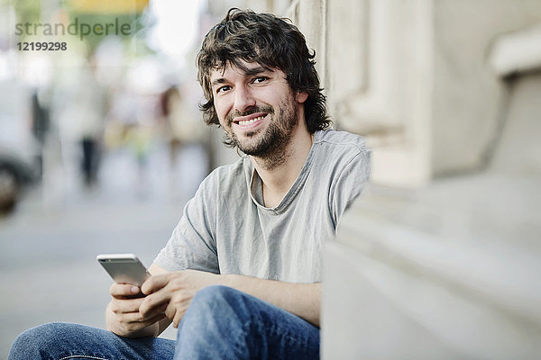 Portrait eines lächelnden jungen Mannes mit Handy im Freien