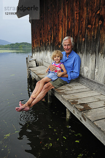 Kleines Mädchen sitzend mit Großvater am Steg im Sommer