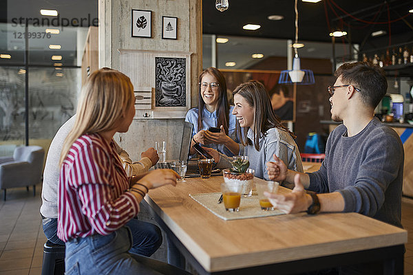Gruppe von glücklichen Freunden sitzen zusammen in einem Café mit Laptop  Smartphone und Getränken.