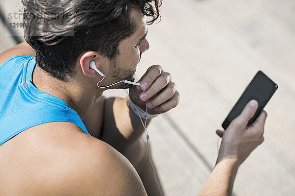 Läufer mit Kopfhörern  der Nachrichten auf seinem Smartphone abruft