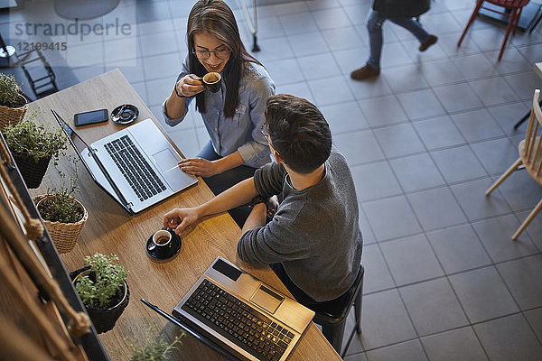 Junge Frau und Mann in einem Café mit Laptops reden und Espresso trinken