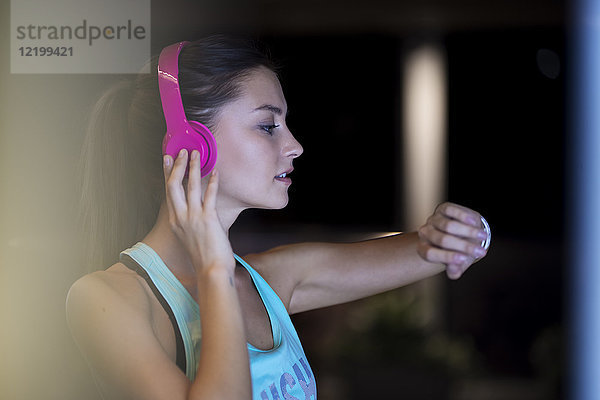 Junge Frau mit rosa Kopfhörern überprüft ihre Smartwatch