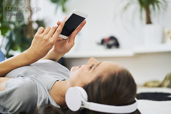Junge Frau auf dem Boden liegend mit Kopfhörer und Handy