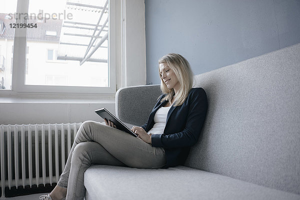 Smling Geschäftsfrau auf der Couch sitzend mit Tablette