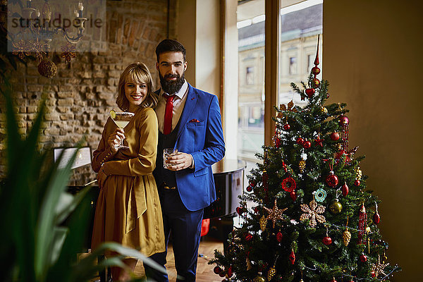 Portrait eines eleganten Paares mit Getränken am Weihnachtsbaum