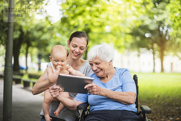 Großmutter  Tochter und Enkelin haben Spaß mit Tablette im Park