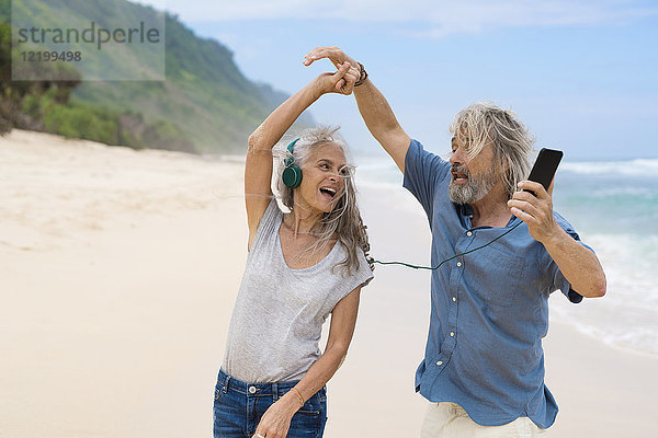 Hübsches Seniorenpaar mit Kopfhörern am Strand tanzend