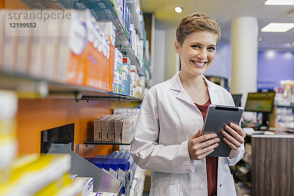 Porträt eines lächelnden Apothekers im Regal mit Medikamenten in der Apotheke mit Tablette
