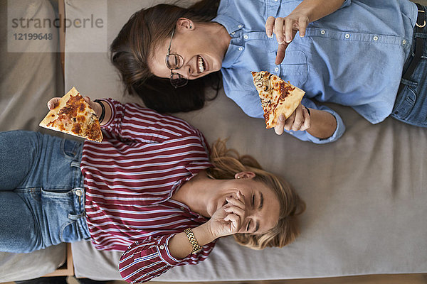 Zwei lachende junge Frauen  die zusammen Pizza essen.