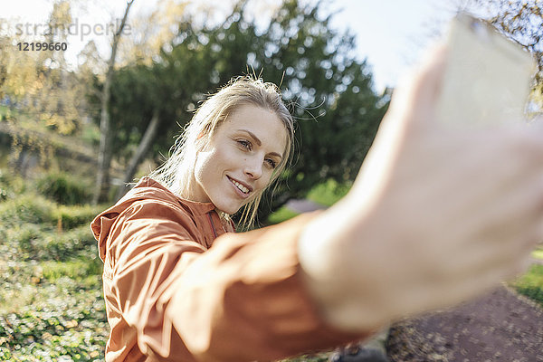 Porträt einer jungen Frau  die sich selbst mit dem Handy im Herbstpark fotografiert.