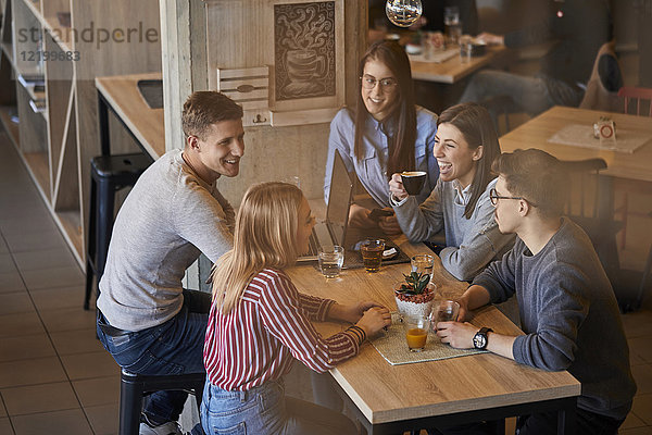 Gruppe glücklicher Freunde  die zusammen in einem Café mit Laptop und Getränken sitzen.
