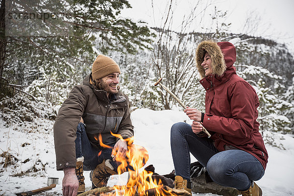 Glückliches Paar auf einer Reise im Winter bei einer Pause am Lagerfeuer
