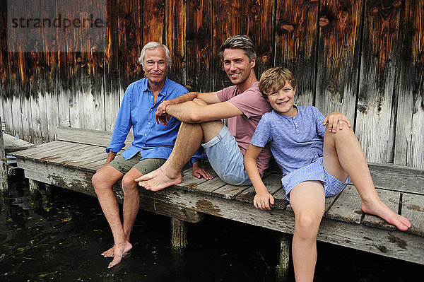 Junge sitzend mit Großvater und Vater zusammen am Steg im Sommer