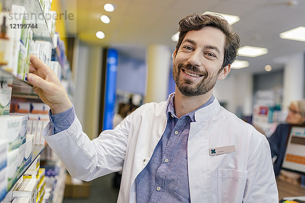 Porträt eines lächelnden Apothekers mit Medikamenten im Regal in der Apotheke