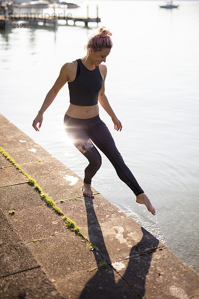 Frau in Sportbekleidung am Seeufer hält den Fuß ins Wasser