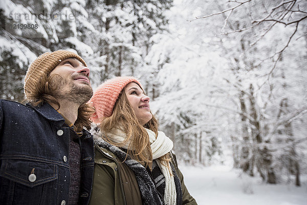 Lächelndes Paar im Winterwald  das den Schneefall beobachtet