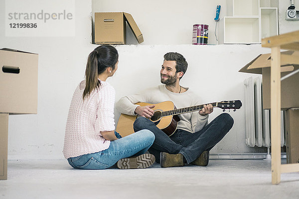 Ein Paar sitzt auf dem Boden und spielt Gitarre.