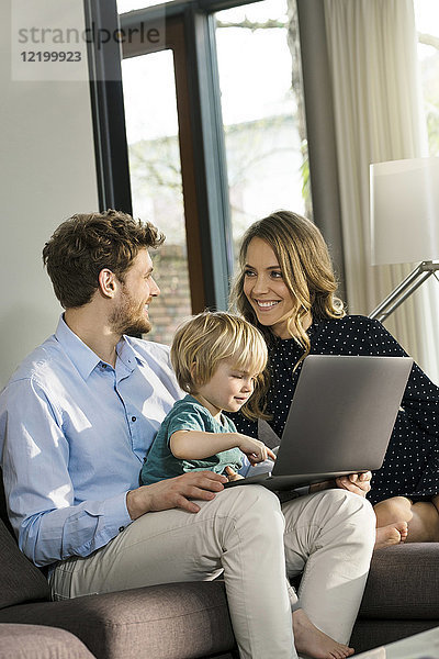 Lächelnde Eltern und Sohn sitzen auf dem Sofa mit dem Laptop zu Hause.