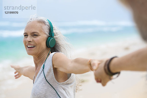 Porträt einer schönen lächelnden Seniorin  die am Strand tanzt.
