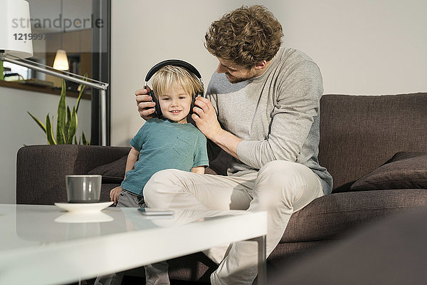 Vater setzt Kopfhörer auf Sohn auf Couch zu Hause auf