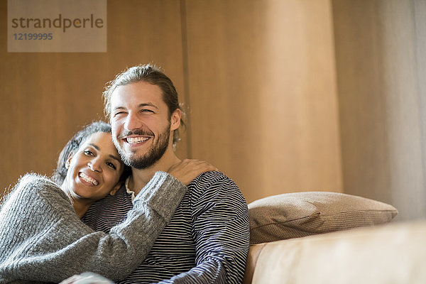 Porträt eines glücklichen jungen Paares  das auf der Couch sitzt.