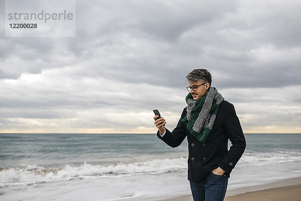 Geschäftsmann am Strand mit Blick aufs Handy