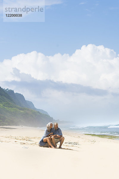 Seniorenpaar am Strand sitzend  in eine Decke gehüllt