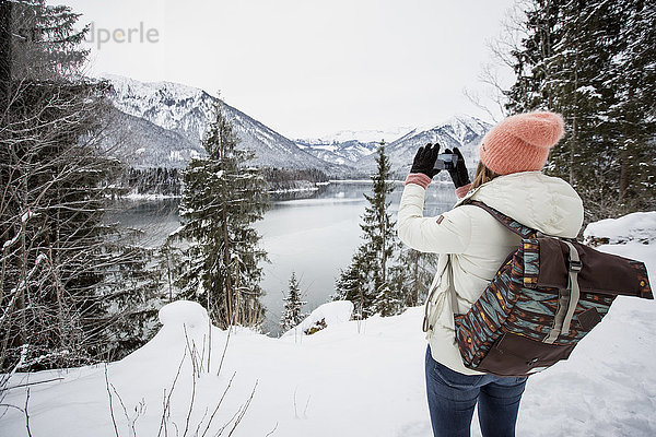 Junge Frau fotografiert in alpiner Winterlandschaft mit See