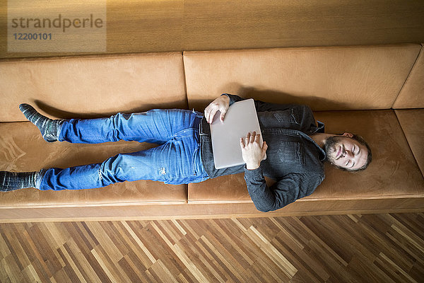 Mann mit Laptop entspannt auf der Couch